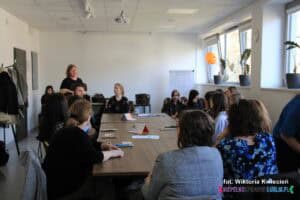 Grupa osób siedzących wokół stołu, w tle stoi prowadząca warsztaty dr hab. Anna Prokopiak, prof. UMCS