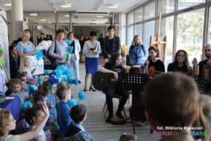 Występ artystyczny zespołu „AUKUSTYCZNI” dla grupy dzieci i dorosłych; w tle w grupie dorosłych stoją Panie Joanna Olszewska oraz Barbara Danieluk