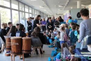 Grupa dzieci i dorosłych zgromadzonych w holu Chatki Żaka podczas występu zespołu „AUKUSTYCZNI”