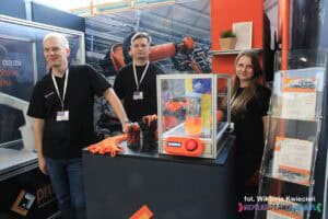 Stoisko firmy PROPOINT S.A. na targach pracy. Trzy osoby stoją obok siebie: dwóch mężczyzn i kobieta. Po prawej stronie znajduje się stojak z ulotkami