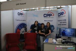 Stoisko firmy CPP Poland na targach pracy wyposażone w dwa czerwone fotele oraz biurko z monitorem. Na stoisku obok siebie stoją trzy kobiety, uśmiechają się do fotografującego
