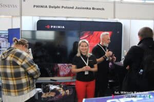 Stoisko PHINIA Delphi Poland Jasionka Branch na targach pracy obsługuje dwoje przedstawicieli. Przed stoiskiem stoją dwie osoby - są odwrócone tyłem, zajęte rozmową lub oglądaniem materiałów promocyjnych