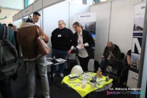 Stoisko firmy Mostostal na targach pracy. Widać sześć osób: dwie z obsługi stoiska i cztery osoby zainteresowane ofertą