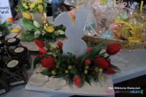 Stroik wielkanocny z białym drewnianym zającem i czerwonymi tulipanami na stoisku Warsztatów Terapii Zajęciowej w Bobrowej Woli