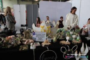 Stoisko Warsztatów Terapii Zajęciowej przy Stowarzyszeniu 'Radość' w Dębicy na Targach Pracy. Widać różnorodność rękodzieła i ozdób wielkanocnych. W obrębie stoiska znajduje się sześć osób