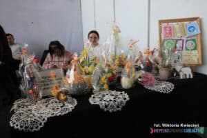 Stoisko Warsztatów Terapii Zajęciowej Caritas Diecezji Rzeszowskiej na Targach Pracy. Widać różnorodność ozdób wielkanocnych i szydełkowych serwetek. W obrębie stoiska znajdują się trzy osoby