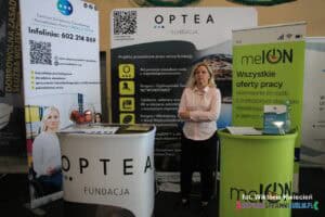Na Targach Pracy, pomiędzy stanowiskami Fundacji Optea oraz melON, stoi kobieta