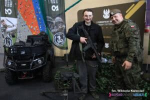 Stoisko 3 Podkarpackiej Brygady Obrony Terytorialnej na Targach Pracy. Pozuje dwóch mężczyzn: cywil prezentujący karabin oraz drugi mężczyzna w mundurze wojskowym.