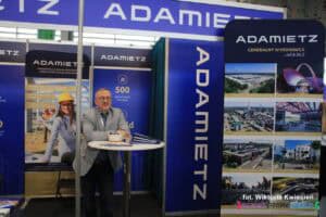 Na Targach Pracy mężczyzna stoi przy wysokim, okrągłym stoliku na stoisku firmy Adamietz