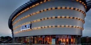 Nowoczesny budynek z zakrzywioną, oświetloną fasadą i dużymi oknami. Na jego konstrukcji widoczny jest tekst 'STYLOWY Centrum Kultury Filmowej' w niebieskich literach.