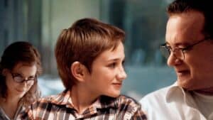 Młody chłopiec uśmiecha się do starszego mężczyzny w okularach. W tle widać kobietę w okularach, patrzącą na nich