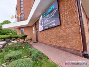 Elewacja kościoła z czerwonej cegły, na której zamontowano nowoczesny ekran multimedialny