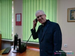 Ksiądz kanonik dr Waldemar Sądecki, proboszcz parafii we wnętrzu Kancelarii; unosi do góry rękę ze słuchawką systemu pętli indukcyjnej