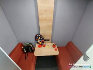 Wnętrze kabiny akustycznej, przypomina miniaturowy przedział kolejowy, wyposażony w niewielkie siedzenia po obu stronach drewnianego stolika