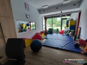 Wnętrze sali wyposażonej w elementy wspierające rozwój ruchowo-sensoryczny. Na ścianie po lewej stronie wmontowano okno fenickie, umożliwiające obserwację pracy z dzieckiem bez jej zakłócania