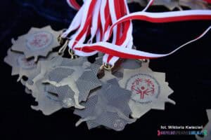 Metalowe medale w nieregularnym kształcie, w kolorze ciemnego złota, na biało-czerwonych tasiemkach. Zawierają sylwetkę piłkarza i napis upamiętniający 'Regionalny Mityng Piłki Nożnej Olimpiad Specjalnych. Lublin, 7 maja 2025 r.'