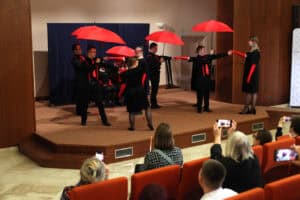 Na scenie artyści podczas tańca z czerwonymi parasolami