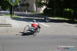 Zawodnik na handbike’u z numerem 378 skręca z ulicy Marii Curie-Skłodowskiej w Grottgera. Przed nim widoczny inny zawodnik na trasie