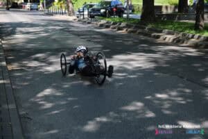Zawodnik na handbike’u w kasku i stroju sportowym porusza się po jezdni ulicy Marii Curie-Skłodowskiej