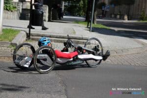 Zawodnik na handbike’u w kasku i stroju sportowym. Tył pojazdu oznaczony numerami startowymi 363 i 63