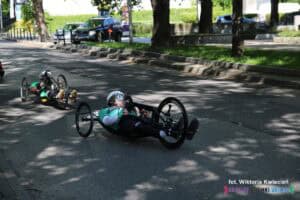 Dwóch zawodników na handbike'ach poruszających się wzdłuż ulicy Marii Curie-Skłodowskiej