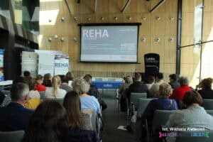 Sala konferencyjna - widok z widowni. Na ścianie ekran multimedialny z wyświetloną powitalną planszą z nazwą konferencji