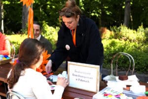 Widok na stolik Środowiskowego Domu Samopomocy w Puławach. Warsztat tematyczny: ozdabianie kartek okolicznościowych. Na zdjęciu dziecko wykonujące kartkę pod okiem pań z ww. instytucji