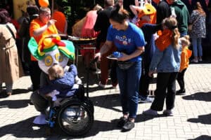 W centralnej części kadru dziecko na wózku przytulające bajkową postać z Psiego Patrolu. Obok wolontariuszka Aniołów Dobroci