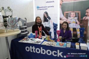 Stoisko firmy ottobock, za stołem siedzą kobieta i mężczyzna; na stoliku ekspozycja ortopedyczna oraz materiały informacyjne