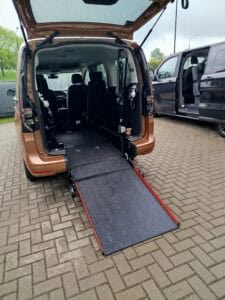 Wnętrze samochodu typu VAN marki Volkswagen z podniesionymi tylnymi drzwiami i opuszczoną platformą dla wózków inwalidzkich