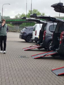 Trzy samochody ustawione w szeregu z podniesionymi tylnymi drzwiami i opuszczonymi platformami umożliwiającymi wjazd wózkom inwalidzkim