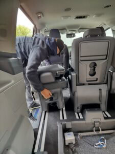 Mężczyzna pochylony nad fotelem pasażera wewnątrz samochodu, montuje siedzisko