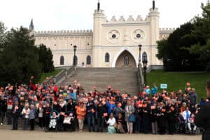 Zgromadzeni goście pozują do zdjęcia z pomarańczowymi chorągiewkami na tle Muzeum Narodowego w Lublinie