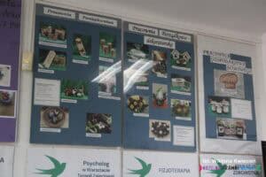 Zdjęcia przedmiotów wykonanych w pracowniach: pamiątkarstwa, porządkowo-dekoratorskiej i gospodarstwa domowego, umieszczone w szklanych antyramach na ścianie.