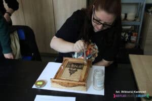 Uczestniczka lakieruje własnoręcznie wykonaną, drewnianą skrzyneczkę z wypalonym wizerunkiem Bramy Krakowskiej i napisem „Lublin”