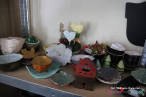 Na półce stoją różnokolorowe, szkliwione przedmioty użytkowe wykonane w pracowni ceramicznej