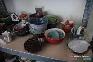 Na półce stoją różnokolorowe, szkliwione przedmioty wykonane w pracowni ceramicznej, przeważają miseczki