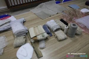 Na stole rozłożone są materiały o różnych fakturach, przygotowane na warsztaty rękodzielnicze