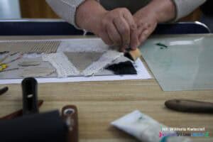 Zbliżenie na dłonie pokrywające powierzchnię matrycy do kolografii farbą drukarską przy pomocy małej gąbeczki