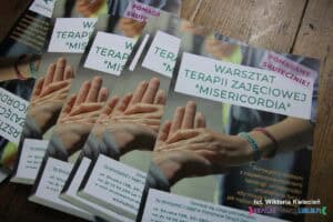 Zbliżenie na ulotki Warsztatu Terapii Zajęciowej ułożone na drewnianym podłożu