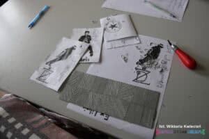 Na stole w pracowni komputerowo-poligraficznej leżą kartki z grafikami exlibrisów oraz rozpoczęta płytka linorytu wraz z dłutkiem i opiłkami