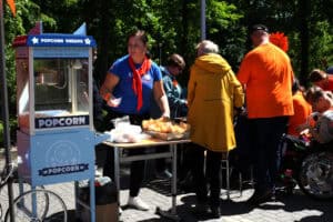 Widok na uczestników uroczystości i jedną z atrakcji: maszynę do popcornu, przy której stoi wolontariuszka Aniołów Dobroci