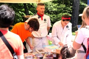 Robienie pizzy pod okiem profesjonalistów z Bravo Chef! Widok na prowadzących warsztaty i młodego człowieka, który nakłada dodatki na pizzę