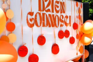 „Ścianka” do fotografii z pomarańczowym napisem Dzień Godności, pomarańczowymi balonami i zawieszkami z wypisanymi przez uczestników sentencjami i pozdrowieniami