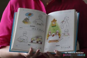 Wnętrze słownika pt. „Szkolny słownik języka migowego, Tom I” autorstwa Bogdana Szczepankowskiego i Marka Rony. Na lewej stronie rozrysowano obrazkowo wyrazy „głodny” i „bez” (w znaczeniu braku), a na prawej stronie znajduje się wyraz „obiad”. Zamieszczono także daktylogramy tych wyrazów, czyli znaki migowe odpowiadające poszczególnym słowom