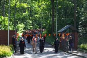 Wejście pierwszych uczestników marszu na teren fundacji. Symboliczne przejście pod pomarańczową wstęgą, na której powiewają pomarańczowe proporce