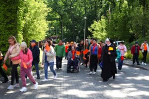Uczestnicy marszu z pomarańczowymi chorągiewkami wchodzą na teren fundacji. Na pierwszym planie siostra zakonna z pomarańczową chorągiewką
