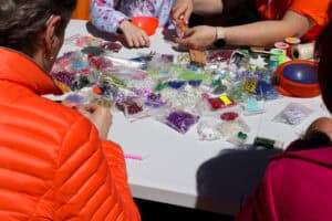 Jeden z warsztatów tematycznych. Na zdjęciu robienie bransoletek z kolorowych koralików. Na stoliku wyeksponowano woreczki z koralikami