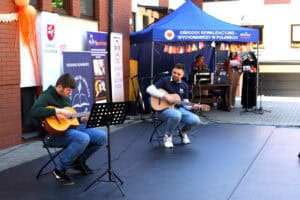 Artysta prezentuje utwór na gitarze, w asyście osoby wspomagającej. W tle stoisko techniczne Ośrodka Rewalidacyjno – Wychowawczego w Puławach