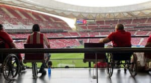 Fani na wózkach oglądają mecz piłkarski z dostępnej strefy widokowej w dużym, zatłoczonym stadionie.